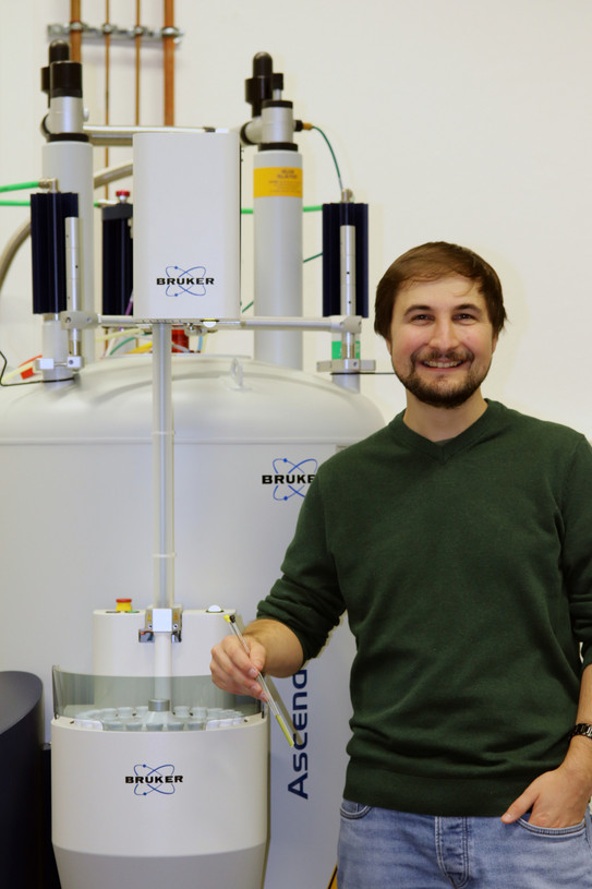Portrait of André Platzek in front of a Bruker 500MHz NMR