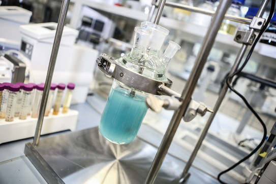 Detailaufnahme Probengefäß im Labor_04 Ein Probengefäß mit hellblauer Flüssigkeit ist fest eingespannt in einer Metallhalterung.